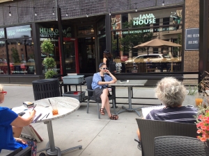 An artist's model poses at a coffee shop sidewalk table while being sketched by class members in downtown Iowa City