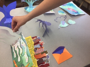 A workshop participant selects colorful paper shapes to add to a three-dimensional artwork