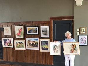 Jo Myers-Walker poses with paintings to add to the IWS 2019  Annual Exhibition at La Poste in Perry, Iowa