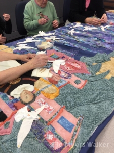 Detail of fabric artwork by artist Jo Myers-Walker showing several people assisting in the placement of fabric doves