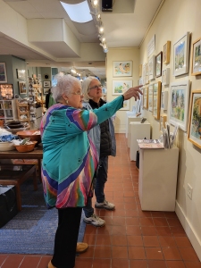Artist Jo Myers-Walker point to a painting while talking with an attendee of November 2022 show opening at Iowa Artisans Gallery