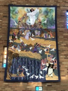 Fabric wall hanging by artist Jo Myers-Walker depicting scenes from the Easter story, revised to emphasize the figure of Jesus, shown on display at St. Thomas Aquinas Church