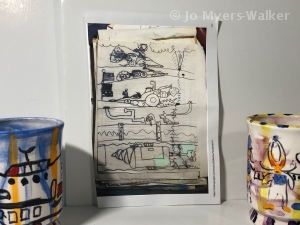 A black-and-white image of a child's drawings together wtih colorful mugs designed using the drawings