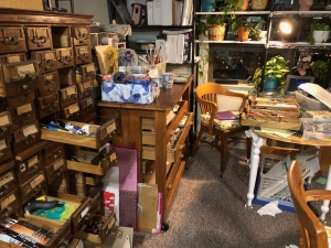 Busy living room with wooden furniture against the wall at left, with many drawers for storage, some of which are open partway to show their contents